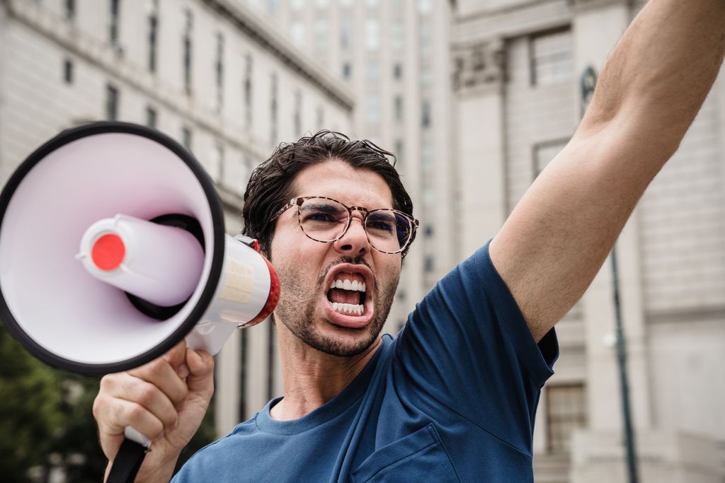 A man energetically shouting through a megaphone during a city protest.