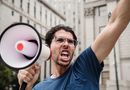 A man energetically shouting through a megaphone during a city protest.
