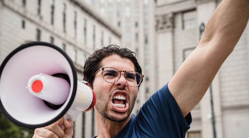 A man energetically shouting through a megaphone during a city protest.