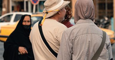 Back view of pedestrians walking on city sidewalk, showcasing diverse attire and urban life.