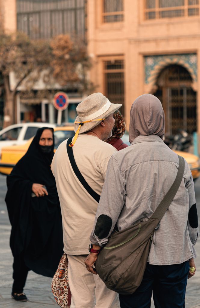 Back view of pedestrians walking on city sidewalk, showcasing diverse attire and urban life.