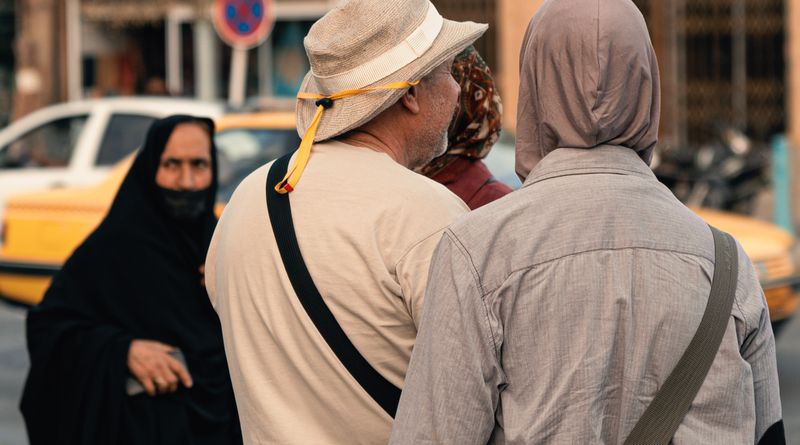 Back view of pedestrians walking on city sidewalk, showcasing diverse attire and urban life.