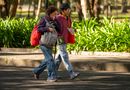 Casual couple strolling through a lush green park during the day, surrounded by trees and foliage.