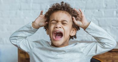 Despaired African American boy with curly hair and closed eyes screaming while standing in light room at home near wall