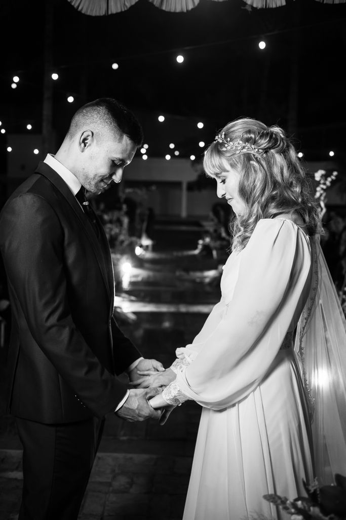 Intimate black and white wedding moment with bride and groom sharing vows under twinkling lights.