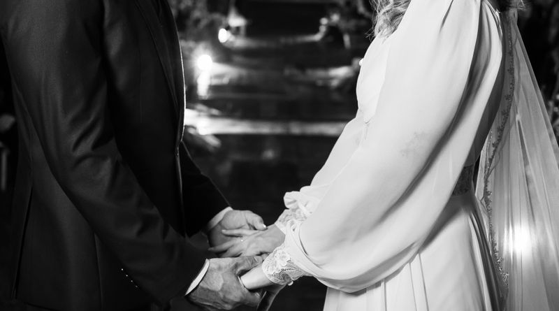 Intimate black and white wedding moment with bride and groom sharing vows under twinkling lights.