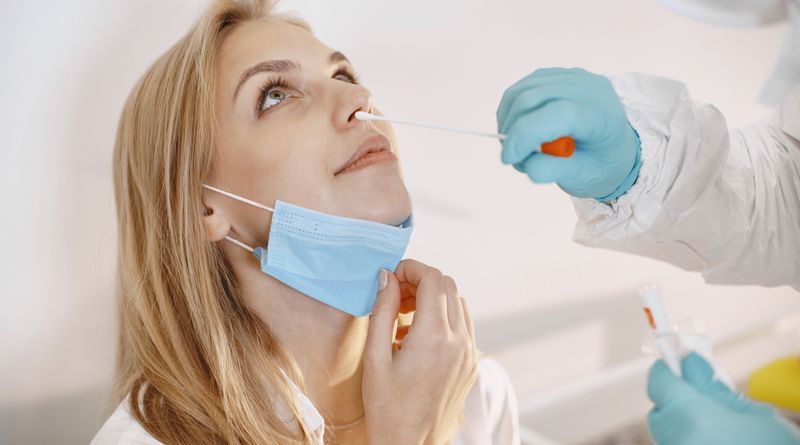 Medical professional performing a COVID-19 nasal swab test on a patient wearing a face mask.