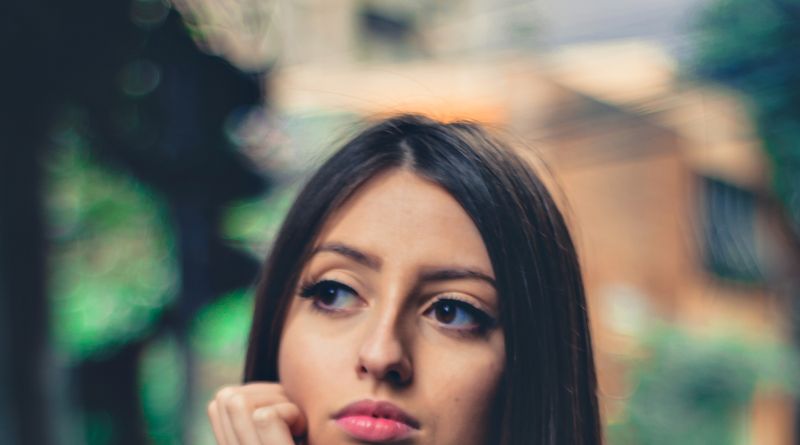 Portrait of a pensive brunette woman in casual attire sitting at an outdoor table.