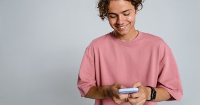 Teenager with curly hair smiling down at smartphone in a studio setup.