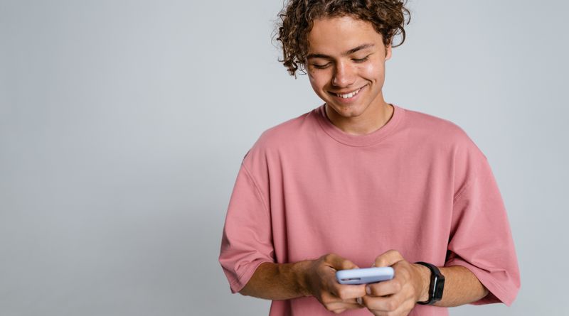Teenager with curly hair smiling down at smartphone in a studio setup.