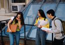 Three students sharing a laugh while standing outside a university building. Perfect for education and campus life themes.