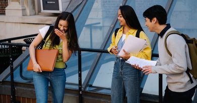 Three students sharing a laugh while standing outside a university building. Perfect for education and campus life themes.