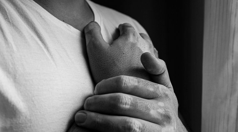 A black and white photo highlighting hands with vitiligo and a heart gesture, emphasizing emotion and diversity.