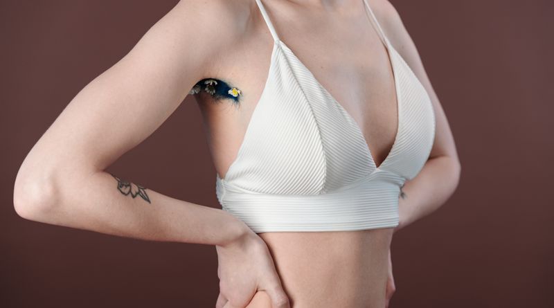 Artistic close-up of a woman's underarm with floral design, wearing a white crop top.