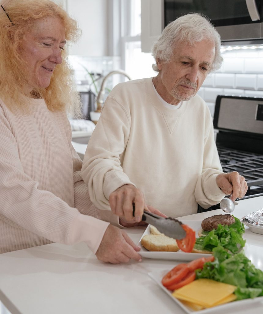 Elderly couple preparing burgers together in a contemporary kitchen setting.