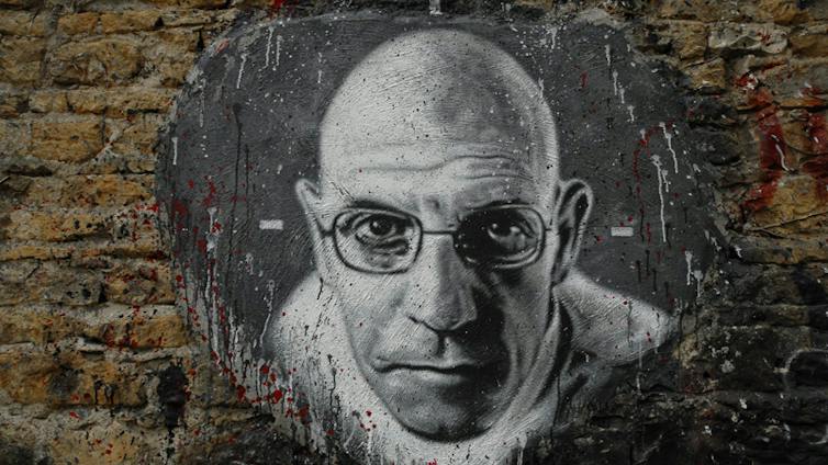 Retrato de la cara de un hombre que aparece en medio de un muro de ladrillo.