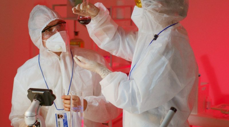 Two scientists in protective suits conduct experiments in a modern laboratory with microscopes and glassware.